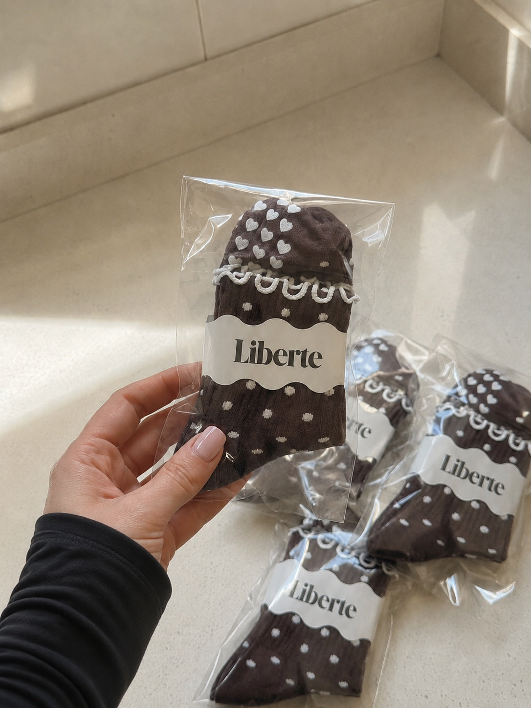 Hand holding packaged Polka Dot Pilates Grip Socks in chocolate brown and cream
